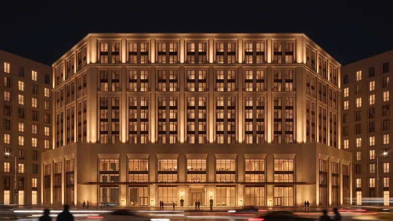 Night render of Gateway Thane, a stone-toned hotel with warmly lit window bays above a lit ground floor, with figures crossing the street in the foreground.