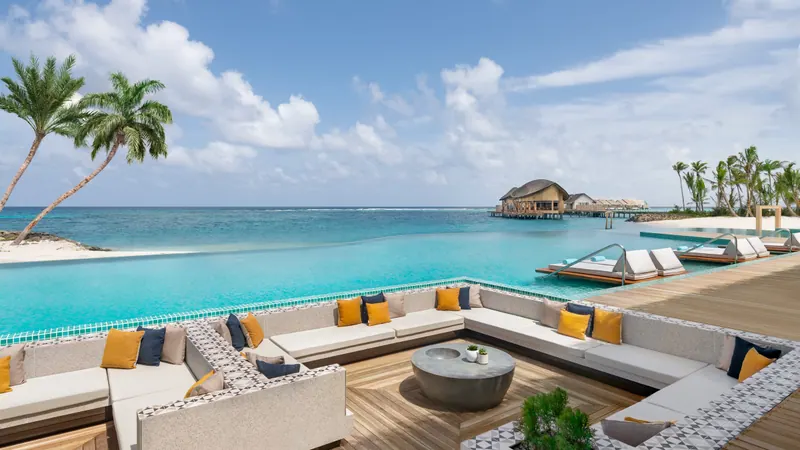 The main pool at Hilton Maldives Amingiri, with a sunken lounge of cushioned seating in the foreground and an infinity edge meeting the turquoise lagoon.